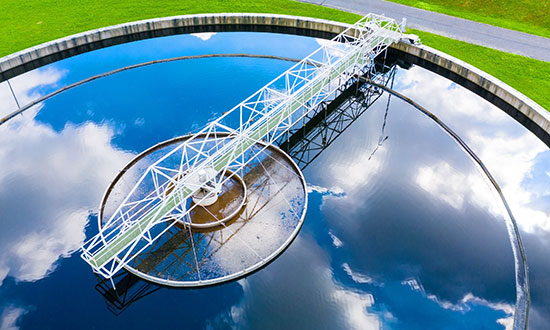 A wastewater treatment tank seen from above, reflecting clouds in the water.